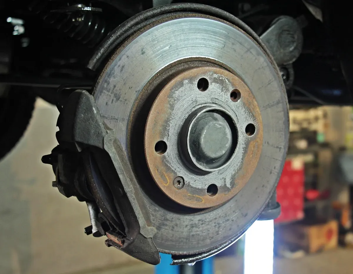 Mechanik wymieniający filtr w samochodzie w profesjonalnym warsztacie z widoczną tarczą hamulcową.